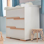 White dresser with wooden accents in a room with blue curtains and a small stool.